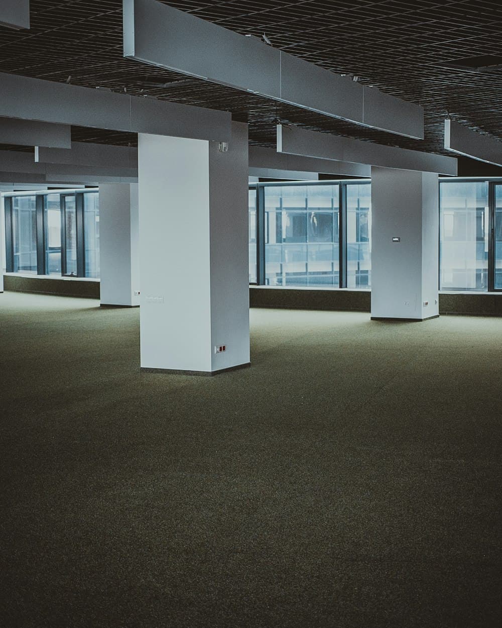 A vacant office floor with square columns and carpet, glazed on two sides.