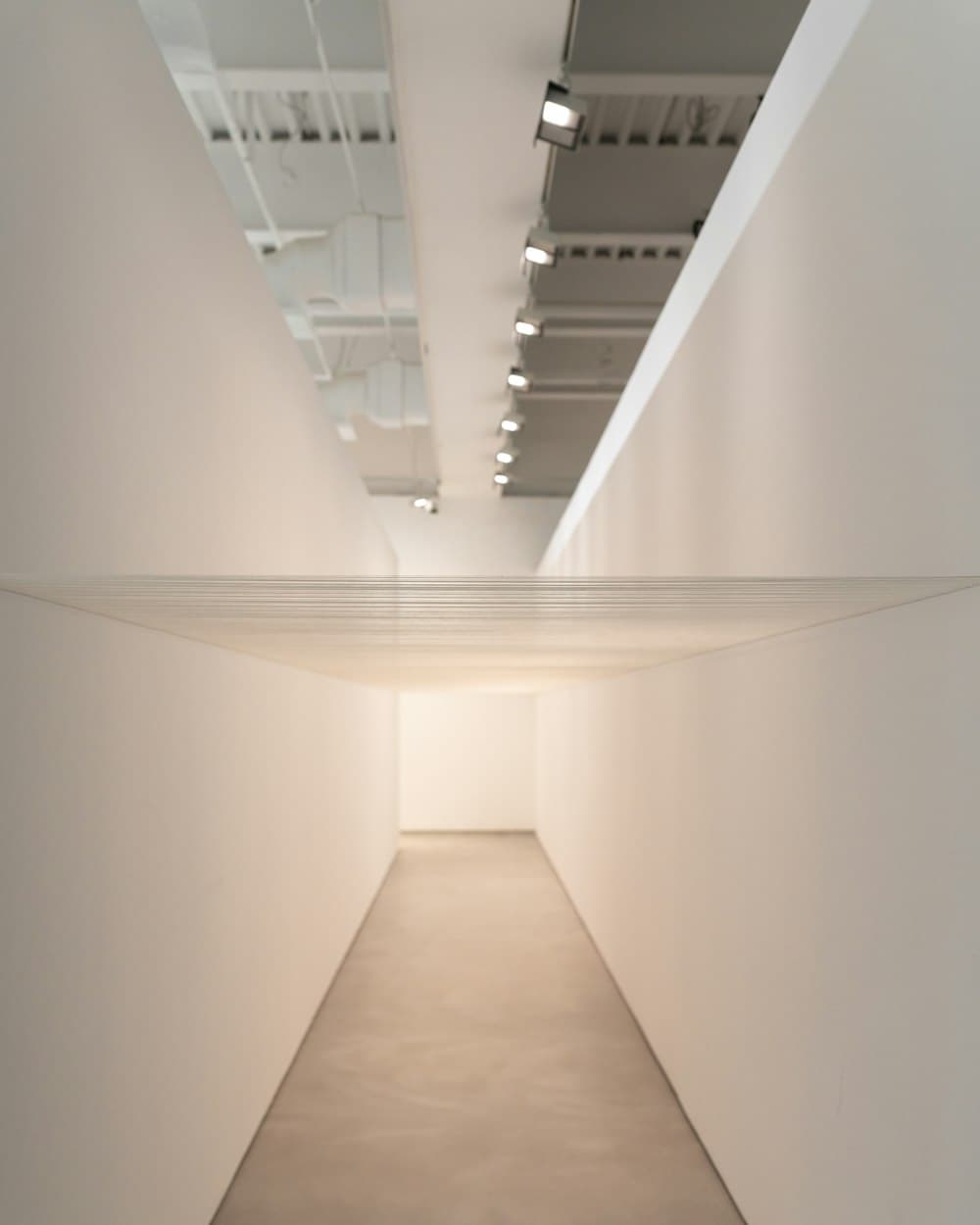 A white gallery corridor lit from a concealed cove, empty, with a doorway at the far end.